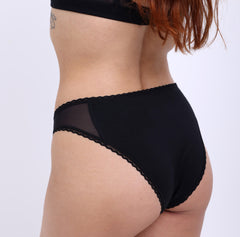 Load image into Gallery viewer, XS Model showing back view of Organic Cotton Black Mid Rise Brief with mesh sides and non-toxic lace detail
Cheeky Coverage