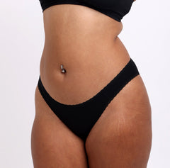 Load image into Gallery viewer, Size M Model showing front and side view of Organic Cotton Black Mid Rise Brief with sexy lace trim detail and mesh sides. Soft, breathable & non-toxic fabric.