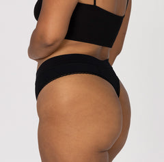 Load image into Gallery viewer, Side and back view of woman wearing all-cotton organic cotton high rise thong style in midnight black, featuring lace detail close up
