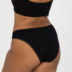 Load image into Gallery viewer, Back/butt view of model wearing mid rise underwear brief style in midnight black all-cotton

