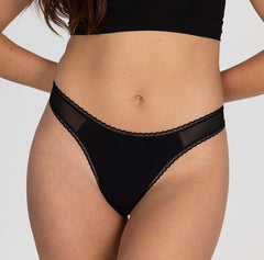 Load image into Gallery viewer, Model showing front view of organic cotton mid rise thong underwear in midnight black, featuring close up of lace detail and mesh panels
