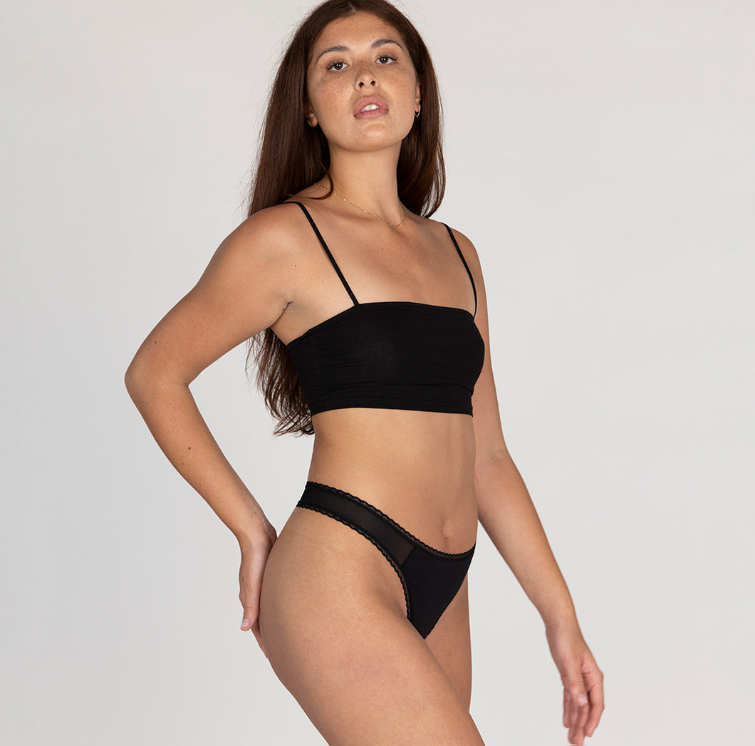 Size small model wearing organic cotton mid rise thong underwear in midnight black, showing lace detail and side high cut leg
