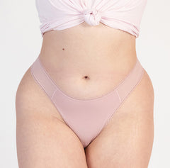 Load image into Gallery viewer, model wearing blush pink organic cotton mid rise thong with high cut sides, wearing blush pink color with mesh panel detail
