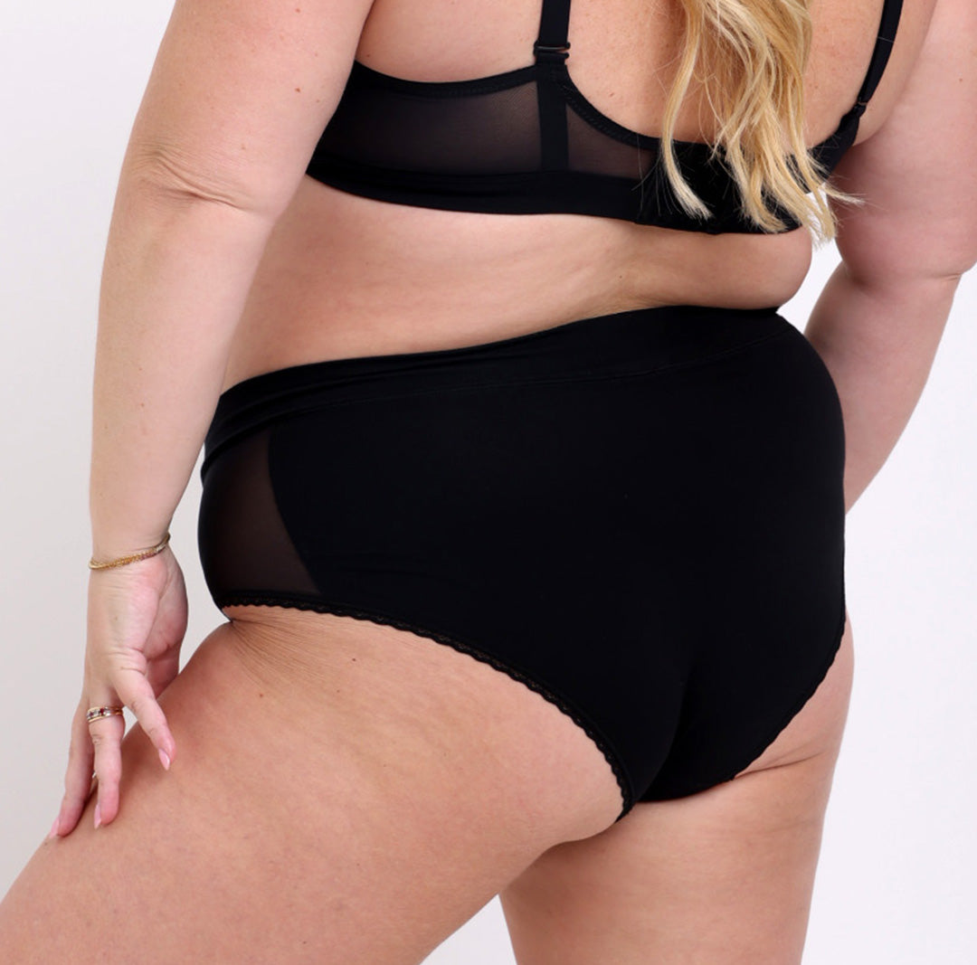 Size 2XL model showing back view of black high rise brief in organic cotton fabric 
No side seams, elastic-free waistband, non-toxic lace trim