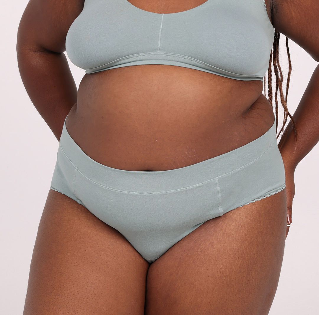 Size 3XL model showing front view of sage high rise brief in certified organic cotton comfy fabric 
No side seams, elastic-free waistband, non-toxic lace trim