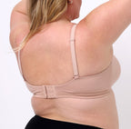 2XL woman showing back of champagne certified organic cotton bralette with adjustable straps and closure.
