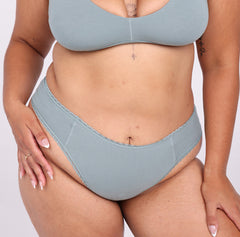 Load image into Gallery viewer, Size L Model showing front view of Certifeid Organic Cotton Sage Mid Rise Brief 
Showing high cut sides and non-toxic lace trim detail

