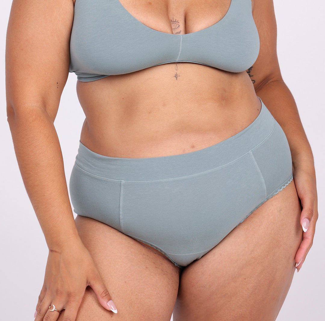 Size L model wearing sage high rise brief in certified organic cotton fabric 
No side seams, elastic-free waistband, non-toxic lace trim