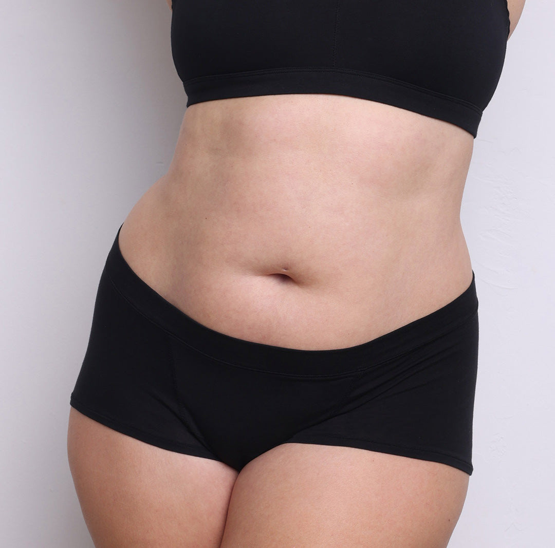 Size L model showing front view of organic cotton mid rise boyshort in midnight black. Soft elastic-free waistband, no front or side seams and full coverage