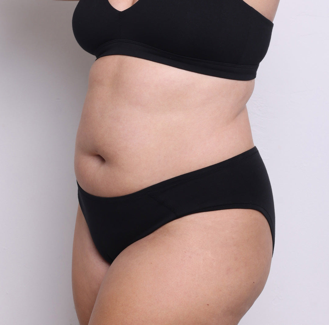Size L model showing front-side view of organic cotton mid rise brief in midnight black. Fuller coverage, never-tight enclosed elastic and a sewn-down longer gusset