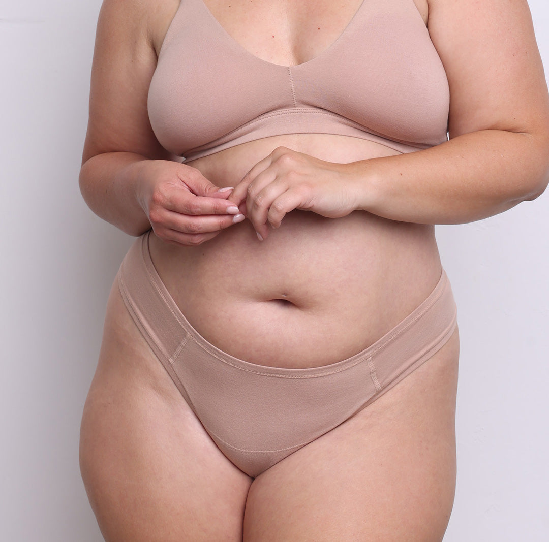 Size L model showing front view of organic cotton dipped front thong in champagne. Dipped mid rise, high-cut leg and never-tight enclosed elastic