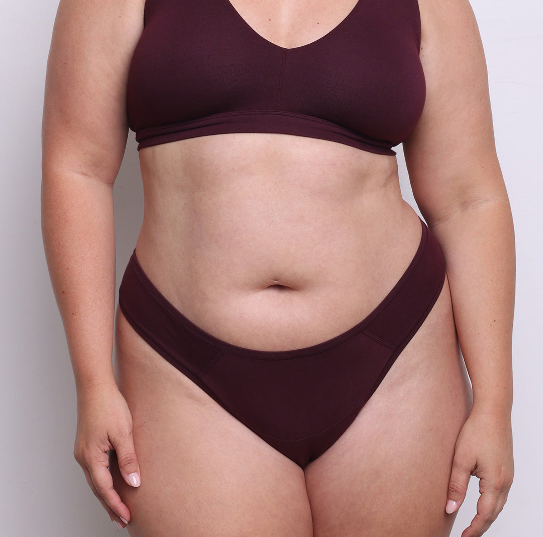 Size L model showing front view of organic cotton dipped front thong in black cherry. Dipped mid rise, high-cut leg and never-tight enclosed elastic