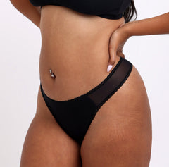 Load image into Gallery viewer, Size M model showing side view of black mid rise thong in organic cotton fabric with mesh panels
Sexy high cut leg, non-toxic lace trim, breathable cotton fabric
