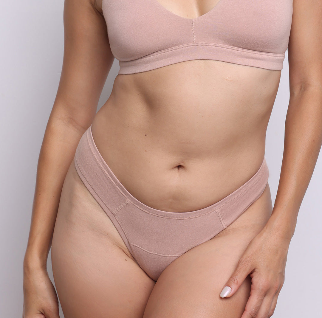 Size S model showing front view of organic cotton dipped front thong in champagne. Dipped mid rise, high-cut leg and never-tight enclosed elastic