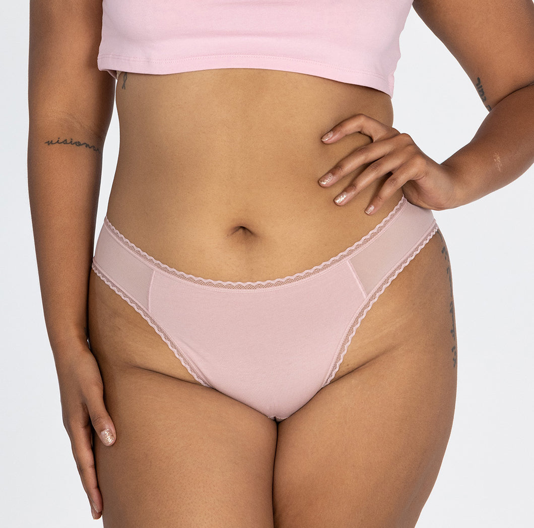 Woman wearing mid rise underwear style in blush pink brief front view, featuring lace detail and high cut leg