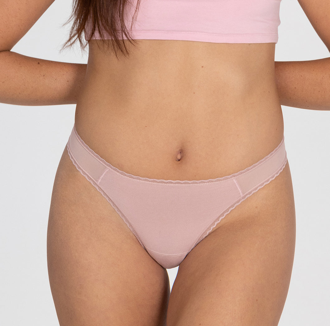 size small model wearing la coochie organic cotton mid rise thong underwear in blush pink, showing lace detail and mesh panels